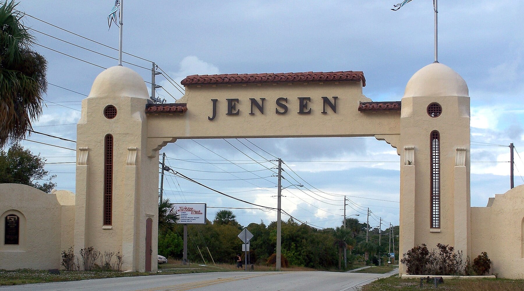 The historic Jensen Beach gateway arch in Jensen Beach, Florida, featuring a cream-colored Spanish-style stucco entrance with a red tile roof and the word "Jensen" displayed across the span.
