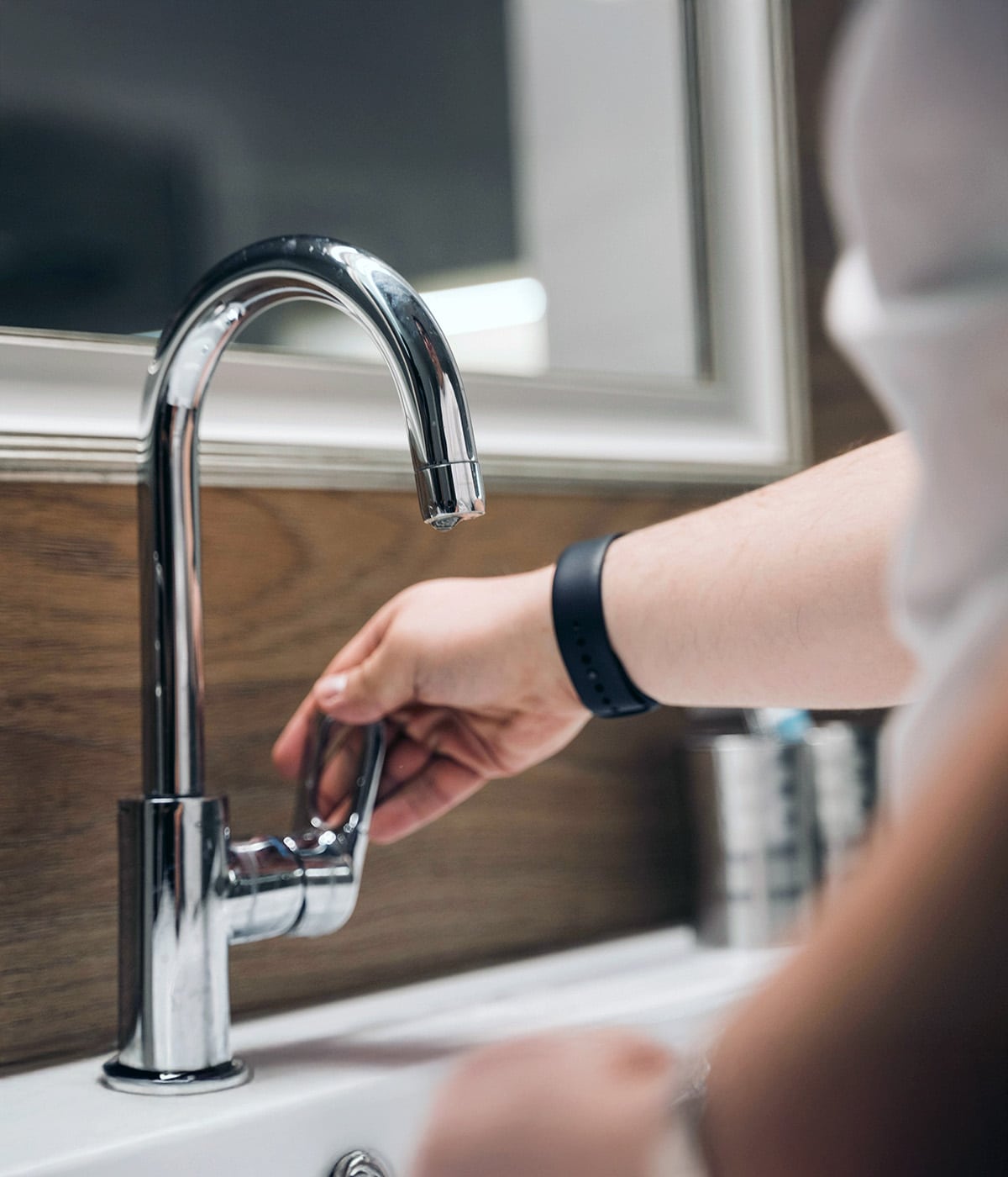 A person turning off a chrome gooseneck bathroom faucet at a white sink